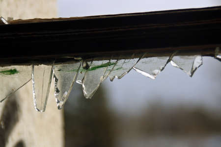Broken window in an abandoned building. Sharp glass debris adhered to the window frame of the broken...