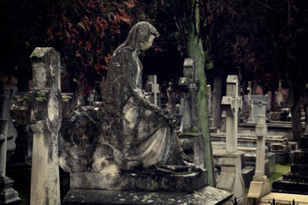 An old statue in a tomb of a catholic cemetery in Madrid, Spain. Weathered statue with lichens due to having been exposed to atmospheric conditions.の写真素材
