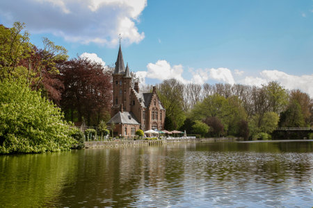 The Greenhouse of Minnewaterpark and the Minnewater lake in Bruges, Belgium. The grove with its foliages of different colors surrounding the main building.の写真素材