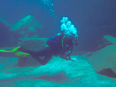 Diver on the bottom and deep blue water. Diver expelling the air in the form of bubbles in Puerto...