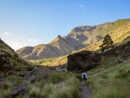 Hiker on the path of the El Risco ravine towards the blue puddle. Gran Canaria Island, Spain. Typical rugged landscape with deep ravines on the island.の写真素材
