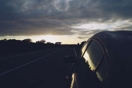 Sunset on the HU-7401 road near Paymogo, Huelva, Spain. Silhouette of trees, a car and the road at...