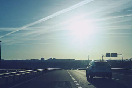 Cars circulating on a highway in Madrid at dawn. The sun rising on the horizon makes driving difficult and creates a backlight effect in the photo. Spain.の写真素材