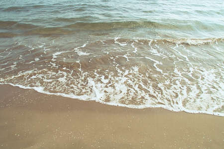 Soft wave with its foam on the golden sand of the Mediterranean Sea. Wave on the Cabanyal beach in...
