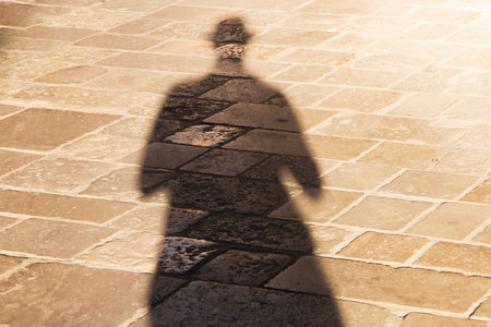 My shadow on the sunny ground of Lecce, Italy. Long shadow of a man with a hat, at sunset on a beige cobbled floor.の写真素材
