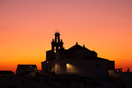 Catholic Church of Our Lady of the Flowers in SanlÃºcar de Guadiana, Huelva, Spain. Silhouette of the church bell tower in an orange sky during sunset.の写真素材