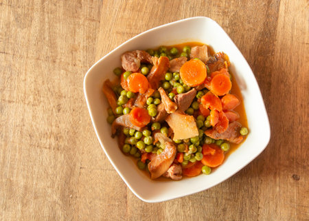 Bowl of turkey stew with peas and wild mushrooms on a wooden table. Healthy food recipe with carrot, peas, onion, saffron milk cap and turkey meat as ingredients. Madrid Spain.の写真素材