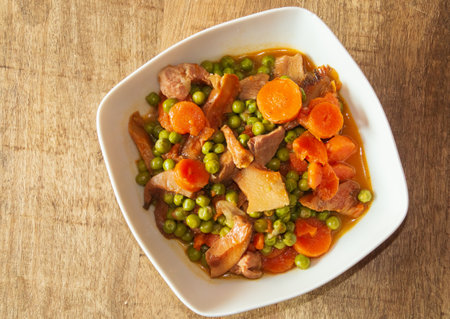 Bowl of turkey stew with peas and wild mushrooms on a wooden table. Healthy food recipe with carrot, peas, onion, saffron milk cap and turkey meat as ingredients. Madrid Spain.の写真素材