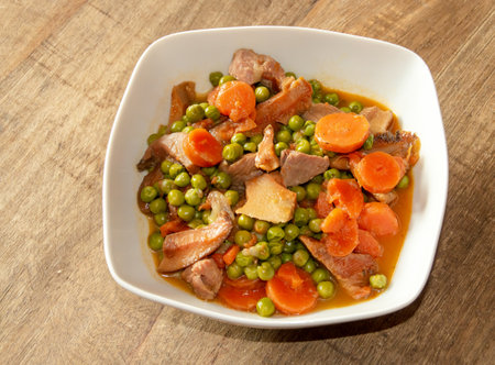 Bowl of turkey stew with peas and wild mushrooms on a wooden table. Healthy food recipe with carrot, peas, onion, saffron milk cap and turkey meat as ingredients. Madrid Spain.の写真素材