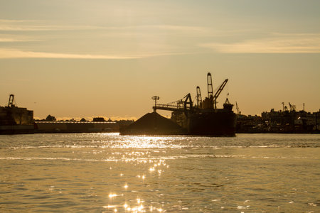 The silhouette of a large cargo ship in the port at sunrise. Industrial and port facilities in Brooklyn along the East River from the Manhattan waterfront in New York, USA.の写真素材