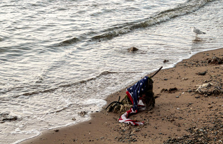 United States flag on the banks of the East River in New York, USA. Old battered flag washed up by the river onto the sandy shore of Manhattan Island.の写真素材