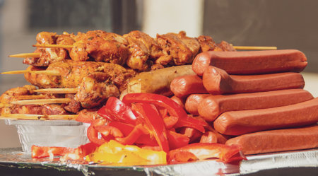 Grilled marinated meat skewers, along with sausages, peppers and tomatoes for hot dogs. Fast food at...