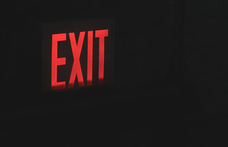 Red exit sign on a glass door in the dark. Illuminated exit sign.の写真素材