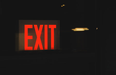 Red exit sign on a glass door in the dark. Illuminated exit sign.の写真素材