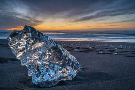 A big block of ice on the beach at sunrise, near the Jokulsarlon lagoon in South Iceland, also...