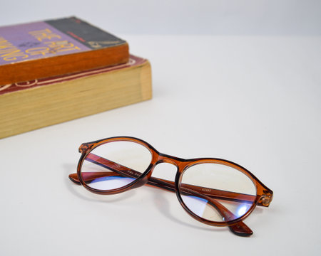 Yogyakarta, Indonesia - January 06, 2023: Glasses for reading against a background of stacks of books. Photographed using a selective focus technique on a white background.のeditorial素材
