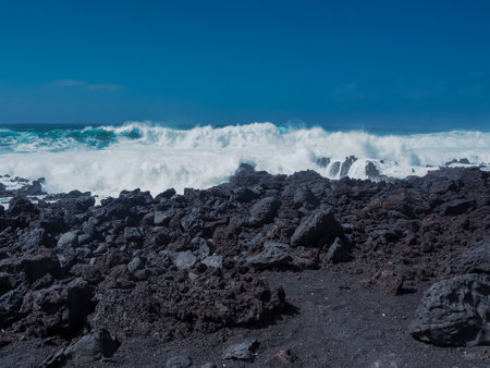 Atlantic waves with white surf meeting the black volcanic coast at El Golfo, Lanzarote, Canary Islands, with a clear blue skyの写真素材