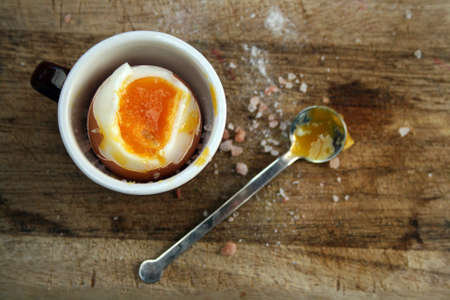 Soft boiled egg, on a wooden board with a spoon and salt view from above.の写真素材