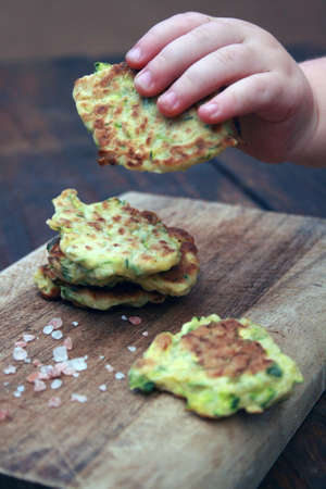 Stack of home made vegetable fritters, with a toddlers hand taking one to eat.の写真素材