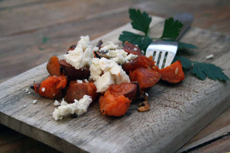 Roasted sweet potato and feta salad with garnish on a wooden board.の写真素材