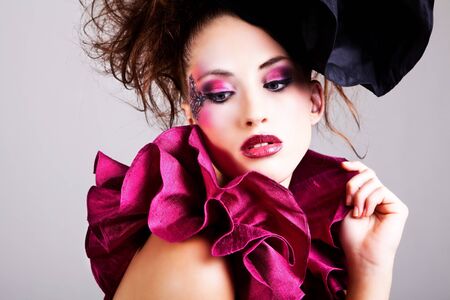 A young woman dressed in avant garde attire. She is wearing a hat and has cosmetic artwork on her right temple. Horizontal shot.の写真素材