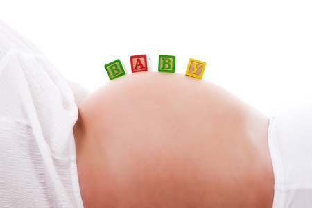 A set of baby blocks spelling out 'BABY' are balanced on the stomach of a pregnant woman. Horizontal shot. Isolated on white.の写真素材
