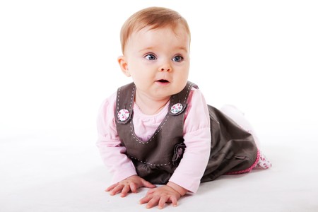 A baby girl is crawling along the floor with an inquisitive look on her face.  Horizontal shot.