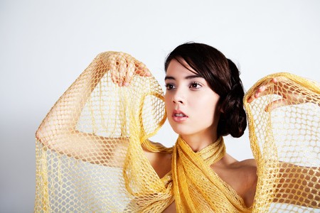 A glamorous, high fashion woman looks to the side while posing in a yellow mesh wrap. Horizontal shot.の写真素材
