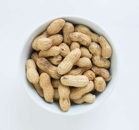 peanut pile in white bowl top view on white background