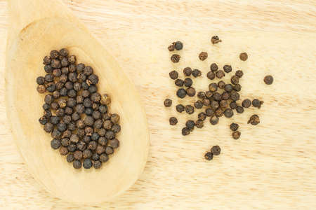 peppercorns in spoon heap on wooden table.の写真素材