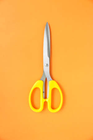 yellow scissors cutting on orange backgroundの写真素材