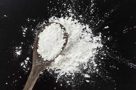 white flour on spoon cooking on black background.