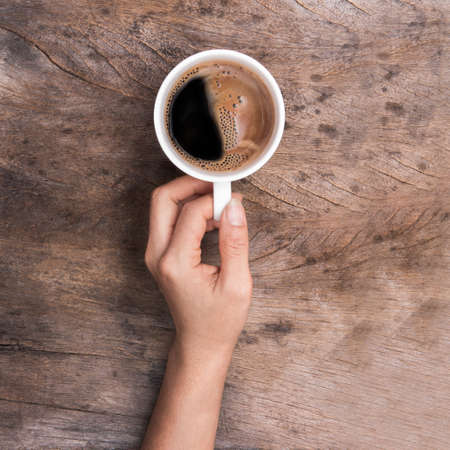 hand holding cup of coffee on wooden tableの写真素材