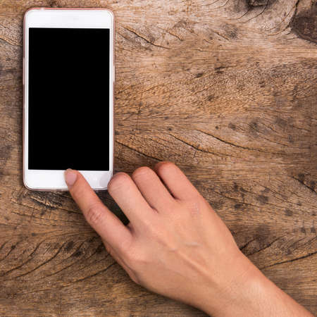 hand pointing home button of smartphone on wooden tableの写真素材