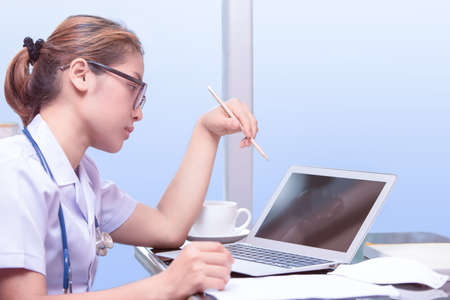 asian doctor woman thinking and considering, doctor holding pencil on left hand with blue stethoscope necklet, asian young doctor working in workroomの写真素材
