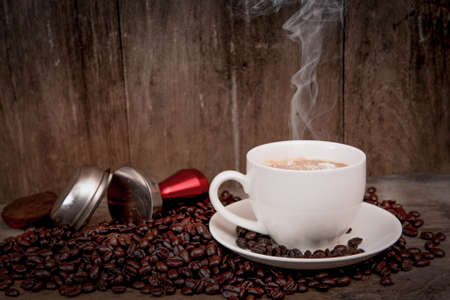 coffee cup with beans on old wooden table and white smoke, coffee beans on wood table and tamper put...