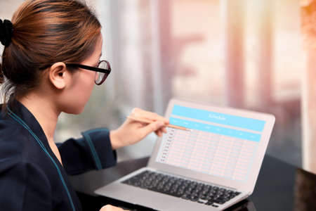 asian women holding and pointing pencil to desktop screen of laptop with schedule on screen, manage work plan by note bookの写真素材