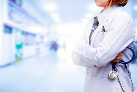 doctor standing and crossed arm with holding blue stethoscope with blurred hospital backgroundの写真素材
