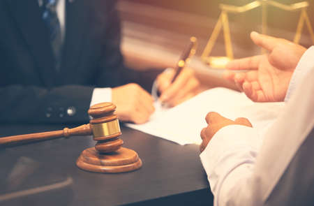 lawyer talking and decision, legal counsel presents to the client a signed contract with judge gavel on wooden desk. justice and lawyer conceptの写真素材