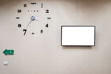 Fire exit sign on wall, fire escape standard sign in building and analog clock and big monitor with white screenの写真素材
