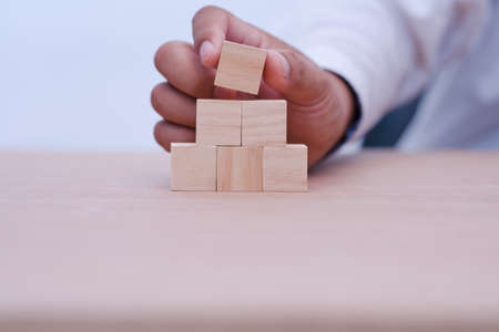 hand holding and arranging wood block stacking as step stair with space for your content in wooden...