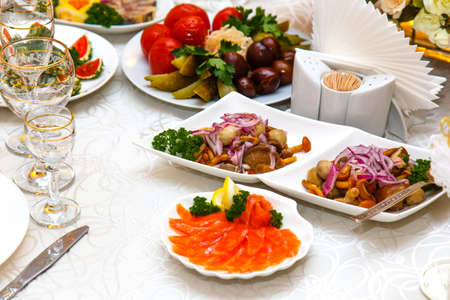 Salad with mushrooms, pickled cucumbers and tomatoes and sliced fish on banquet table