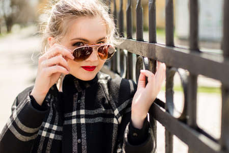beautiful girl in black coat and sunglasses standing near a wrought iron fence