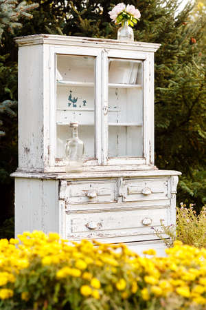 yellow flowers and old white cupboard on a background of firs outdoorsの写真素材