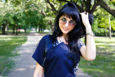 Portrait of a beautiful young brunette girl with long hair walking along the alley in the park