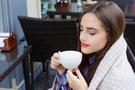 Beautiful young woman wrapped in a blanket holding a cup of tea in an outdoor cafe