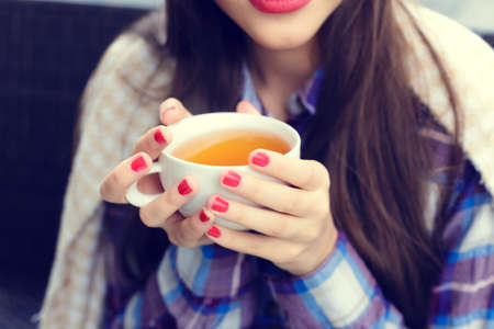 Girl wrapped in a blanket holding a cup of tea close-up in outdoor cafeの写真素材