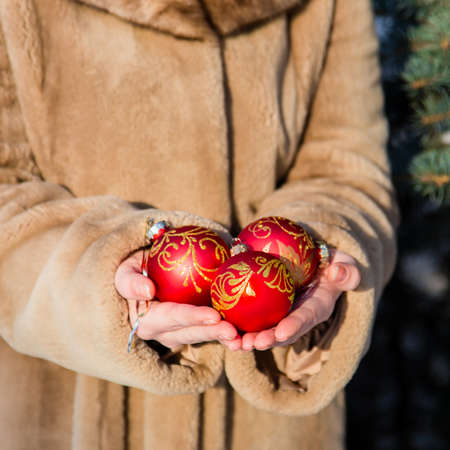 Woman weared in fur coat holding in his hands three red Christmas balls close-up. New Year greeting card conceptの写真素材