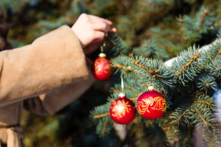 woman dressed in a fur coat hanging a christmas decorations on fir closeup. New year greeting card conceptの写真素材