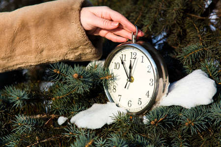 woman dressed in a fur coat hanging a watch on fir closeup. New year greeting card conceptの写真素材